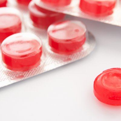 Packets of red coloured throat lozenges on a white background. Adobe